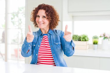 Kıvırcık saçlı, kot ceket giyen, mutlu ve komik yüzlü orta yaşlı bir kadın. İyi enerji ve titreşimler.