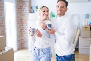 Genç güzel çift karton kutular etrafında yeni evde kahve fincan içme ayakta