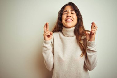 Kışlık süveter giyen güzel bir kadın beyaz izole edilmiş arka plan üzerinde durup umut ve gözlerin kapalı bir şekilde gülümseyerek işaret ediyor. Şans ve batıl inanç..