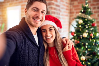 Mutlu ve kendinden emin gülümseyen genç bir çift. Evdeki Noel ağacının etrafında kamerayla selfie çekmek.