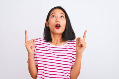 İzole beyaz arka plan üzerinde duran çizgili t-shirt giyen genç Çinli kadın şaşırttı ve yukarı bakarak ve parmakları ile işaret ve kolları kaldırdı şaşırttı.
