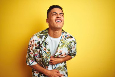 Tatilde olan genç Brezilyalı bir adam, yaz çiçekli gömleğini giyip, el üstünde midesi ağrıyan, hazımsızlık çeken ve kendini kötü hisseden izole edilmiş sarı bir arka plan giyiyor. Ache kavramı.