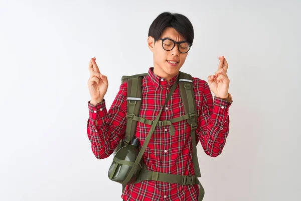 Chinese hiker man wearing backpack canteen glasses over isolated white background gesturing finger crossed smiling with hope and eyes closed. Luck and superstitious concept.