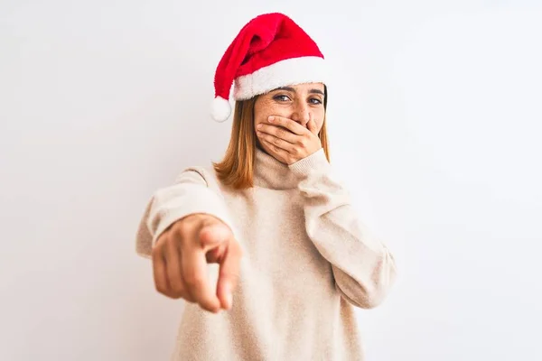 美しい赤毛の女性は 孤立した背景にクリスマスの帽子をかぶってあなたを笑って 口の上に手でカメラに指を向け 恥の表情 — ストック写真