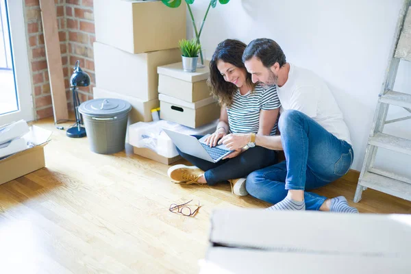 Orta yaş üst düzey romantik çift aşk etrafında kutuları ile daire katında oturan ve bilgisayar laptop kullanarak yeni bir eve hareket için mutlu gülümseyen