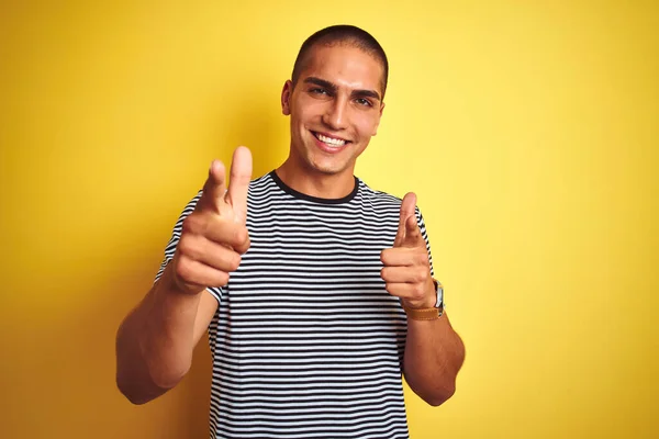 年轻英俊的男子穿着条纹T恤 穿着黄色孤立的背景 手指指向相机 脸上洋溢着欢乐和滑稽的表情 好的能量和活力 — 图库照片