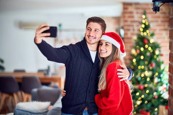 年轻漂亮的夫妇面带微笑 既快乐又自信 在家里的圣诞树下 站着拥抱让自己靠相机拍成电影 — 图库照片