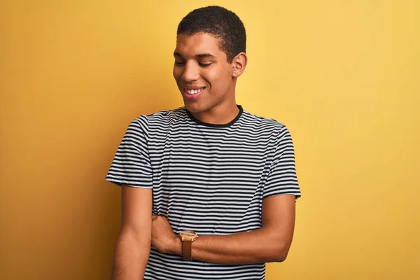 年轻英俊的阿拉伯男子 身穿海军条纹T恤 披着孤立的黄色背景 面带微笑 神态自然地朝一边看去 充满自信的笑 — 图库照片