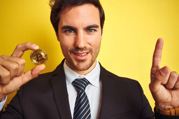 Młody Przystojny Biznesmen Trzymający Bitcoin Stojący Nad Odizolowanym Żółtym Tłem — Zdjęcie stockowe