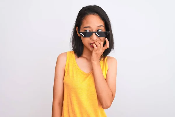 Young beautiful chinese woman wearing thug life sunglasses over isolated white background looking stressed and nervous with hands on mouth biting nails. Anxiety problem.