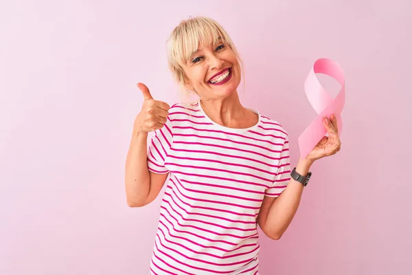 中年女性保持癌リボン上の隔離されたピンクの背景幸せなです大笑顔行いますOkサイン 親指アップとともに指 優れたサイン — ストック写真