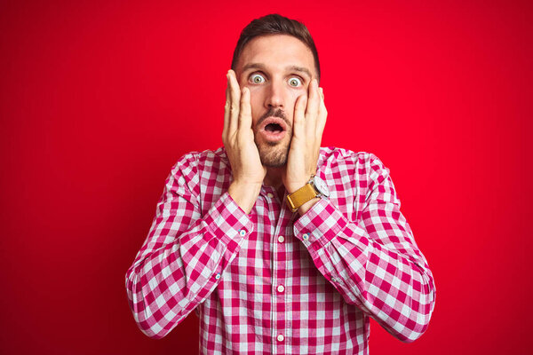 Молодой красивый мужчина на красном изолированном фоне, напуганный и шокированный, удивленный и пораженный выражением лица
