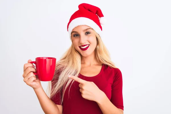 漂亮的女人戴着圣诞圣诞礼帽 站在与世隔绝的白色背景上喝咖啡 手指手画脚 非常高兴 — 图库照片