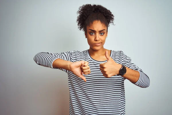 African american woman wearing navy striped t-shirt standing over isolated white background Doing thumbs up and down, disagreement and agreement expression. Crazy conflict