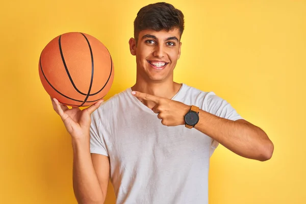 Молодой Индийский Спортсмен Держит Баскетбольный Мяч Стоя Изолированном Желтом Фоне — стоковое фото