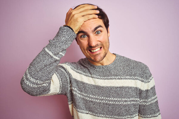 Молодой красивый мужчина в обычном полосатом свитере, стоящий на изолированном розовом фоне, напряженный рукой на голове, шокированный стыдом и удивленным лицом, злой и расстроенный. Страх и разочарование по ошибке
.