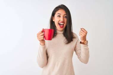 Güzel Çinli kadın kırmızı fincan kahve içiyor. İzole edilmiş beyaz arka planda duruyor. Gururla bağırıyor, zaferi ve başarıyı kutluyor.