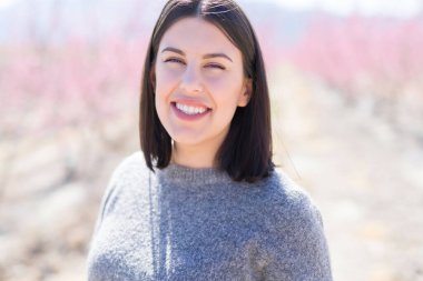 Güzel genç kadın bahar güneşli bir gün pembe yaprakları ile şeftali bahçesinde neşeli gülümseyen