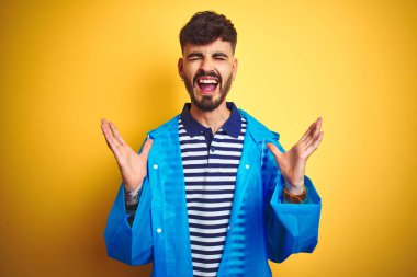 Yağmurluk giyen genç yakışıklı adam izole edilmiş sarı arka planda duruyor. Başarının çılgınlığını kutluyorlar. Kollarını kaldırmış, gözlerini kapatmış heyecanlı çığlıklar atıyorlar. Kazanan konsept