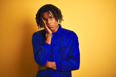 Sarı arka plan üzerinde mekanik üniforma giyen Afro işçi kollarını kavuşturarak depresyondan sıkılmış ve yorgun görünüyor..