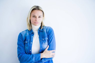 İzole edilmiş beyaz arka plan üzerinde duran kot gömlek giyen genç ve güzel bir kadın şüpheci ve gergin, yüzünde çapraz kollarla onaylamayan bir ifade. Negatif kişi.