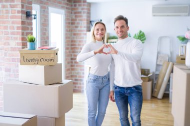 Genç ve güzel bir çift, yeni evlerinde karton kutuların etrafında durup birbirlerine gülümserler. Elleriyle kalp sembolü ve şekli gösterirler. Romantik konsept.