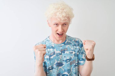 İzole edilmiş beyaz arka plan üzerinde sıradan tişörtler giyen genç albino sarışın adam kollarını kaldırarak ve açık gözlerle başarıyı kutluyor ve şaşırıyor. Kazanan konsept.