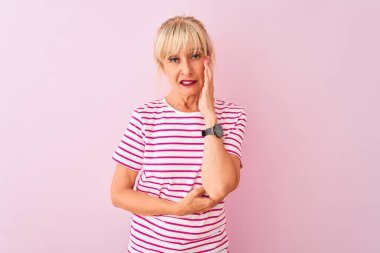 Orta yaşlı bir kadın pembe arka planda duran çizgili tişört giyiyor. Kollarını çapraz tutarak depresyondan sıkılmış ve yorgun görünüyor..