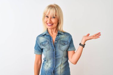 Sıradan bir kot gömlek giyen orta yaşlı bir kadın izole edilmiş beyaz arka planda durup neşeli bir şekilde sunum yapıyor ve avuç içi kameraya bakıyor..