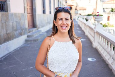 Genç ve güzel bir kadın mutlu bir şekilde gülümsüyor güneşli bir yaz gününde şehir sokaklarında yürüyor.