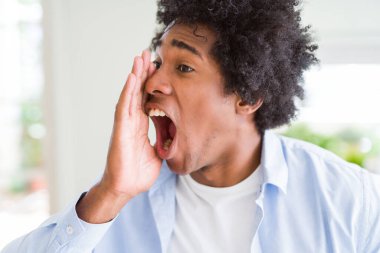 Afro saçlı, eli ağızda bağıran ve yüksek sesle bağıran yakışıklı Afro-Amerikalı adam. İletişim konsepti.