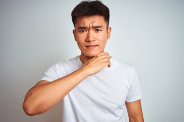 Asyalı genç bir Çinli tişört giyiyor. İzole edilmiş beyaz arka planda duruyor. Bıçak gibi elleriyle boğazını kesiyor.