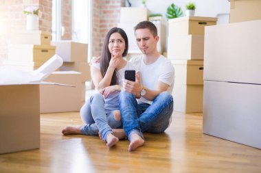 Karton kutuların etrafında akıllı telefonlar kullanarak yerde oturan güzel bir çift. Yüzleri ciddi ciddi soruyla dolu, kafası karışmış bir fikir.