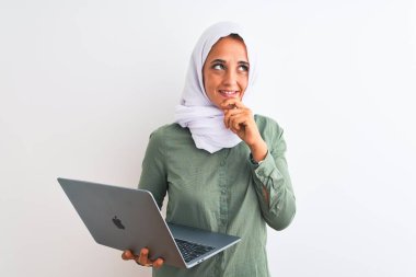 Genç Arap iş kadını tesettür takıyor. Laptop kullanıyor. Tecrit edilmiş arka plan üzerinde. Ciddi bir yüz.