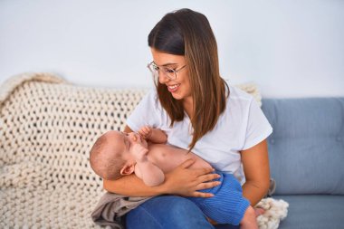 Genç, güzel bir kadın ve bebeği evdeki battaniyenin üzerinde kanepede. Yeni doğan anne rahatlıyor ve dinleniyor.