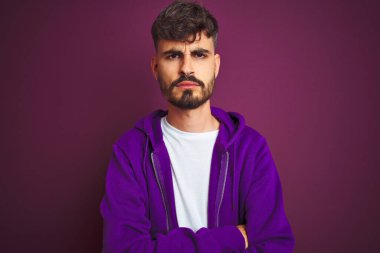 İzole edilmiş sarı arka plan üzerinde duran çizgili polo giyen genç adam şüpheci ve gergin, yüzünde çapraz kollu tasvip etmeyen ifade. Negatif kişi.