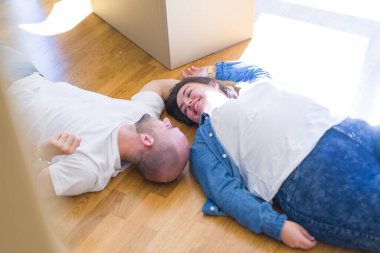 Yeni bir evin katında yatan aşık genç çift, yeni bir daireye taşınmak için çok mutlu gülümseyen, karton kutular civarı