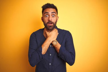 Genç ve yakışıklı Hintli işadamı sarı arka planda gömlek giyip bağırıyor ve boğuluyor çünkü acı verici bir boğulma var. Sağlık problemi. Boğulma ve intihar konsepti.