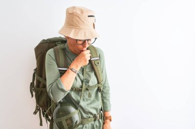 Sırt çantalı matara şapkalı orta yaşlı kadın izole edilmiş beyaz arka planda kendini iyi hissetmiyor ve soğuk algınlığı veya bronşitin belirtisi olarak öksürüyor. Sağlık hizmetleri kavramı.