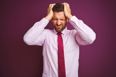 Zarif gömlek ve kravat takan genç iş adamı, mor izole edilmiş arka planda, acı ve migren yüzünden çaresiz ve stresli bir baş ağrısından muzdarip. Ellerini başının üstüne koy..