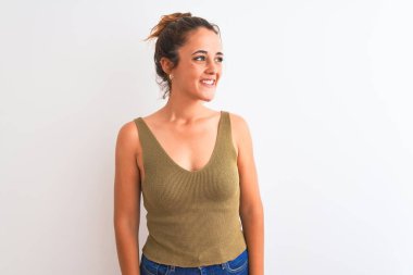 Genç kızıl saçlı bir kadın izole edilmiş arka planda topuz takıyor. Yüzünde gülümseme, doğal bir ifade ile yan yana bakıyor. Kendinden emin gülen.