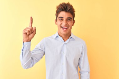 Soyutlanmış sarı arka planda zarif gömlekler giyen yakışıklı genç işadamı başarılı bir fikri işaret ediyor. Heyecanlı ve mutlu. Bir numara..