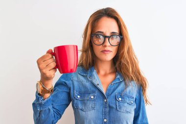 Genç, güzel, kızıl saçlı, gözlüklü, izole edilmiş arka planda bir fincan kahve içen zeki yüzlü, ciddi düşünen bir kadın.