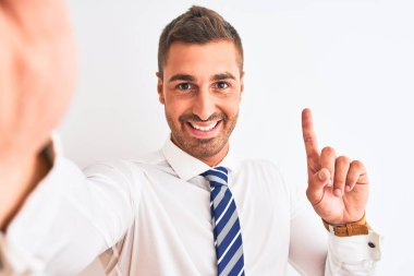 Genç yakışıklı iş adamı, izole edilmiş arka planda akıllı telefon kullanarak selfie çekiyor. Bir fikir ya da soru işareti ile şaşırıyor, mutlu yüzle, bir numara.