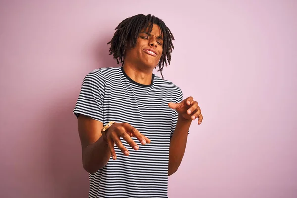 Afro man with dreadlocks wearing navy striped t-shirt standing over isolated pink background disgusted expression, displeased and fearful doing disgust face because aversion reaction. With hands raised. Annoying concept.