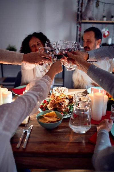 Family and friends dining at home celebrating christmas eve with traditional food and decoration, making a toast with best wishes with glass of wine