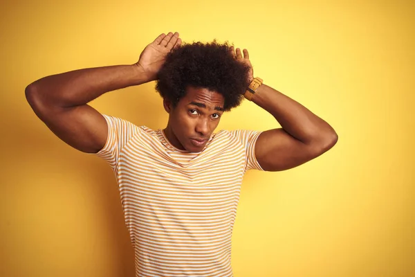 American man with afro hair wearing striped t-shirt standing over isolated yellow background Doing bunny ears gesture with hands palms looking cynical and skeptical. Easter rabbit concept.