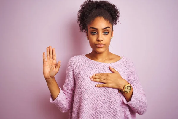Young african american woman wearing winter sweater standing over isolated pink background Swearing with hand on chest and open palm, making a loyalty promise oath