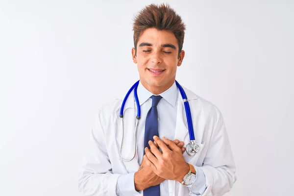 隔離された白い背景に聴診器を身に着けている若いハンサムな医者の男は目を閉じて胸に手で笑顔と顔に感謝のジェスチャー 健康コンセプト — ストック写真