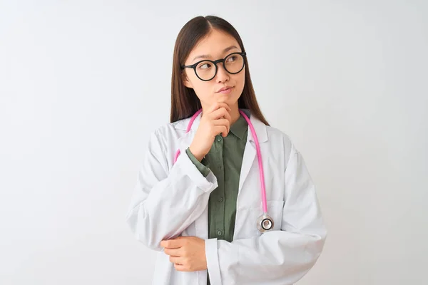 若い中国の医師の女性は 質問について考えてあごの手で隔離された白い背景に眼鏡聴診器を着用し 集中的な表現 思慮深い顔で微笑んだ 疑いの概念 — ストック写真